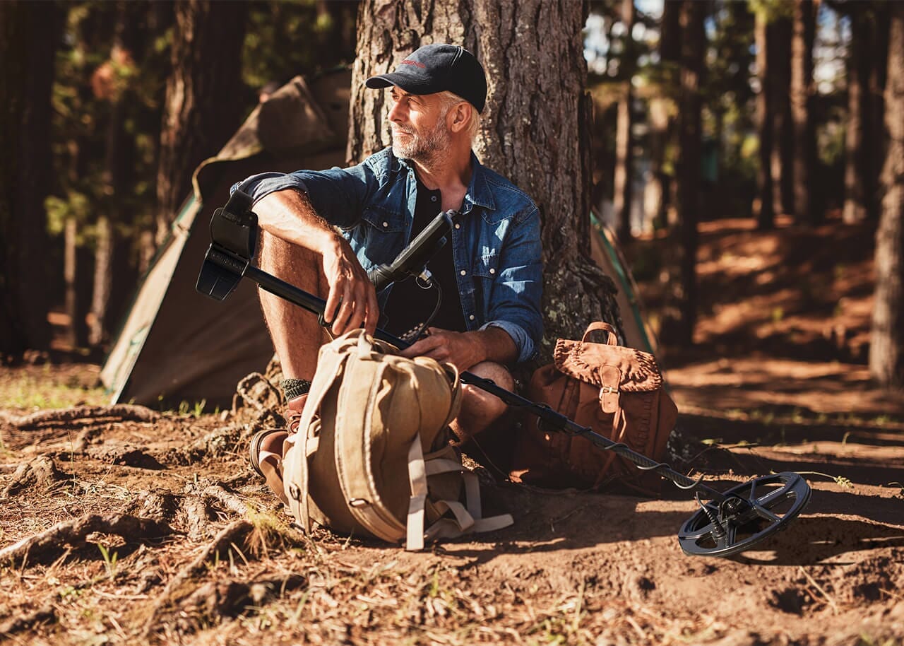 Nokta Legend with 12" x 9" LG30 Coil lifestyle pic man sitting next to tree with metal detector